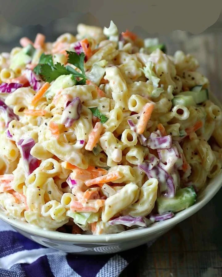 A colorful bowl of coleslaw pasta salad with vegetables and dressing