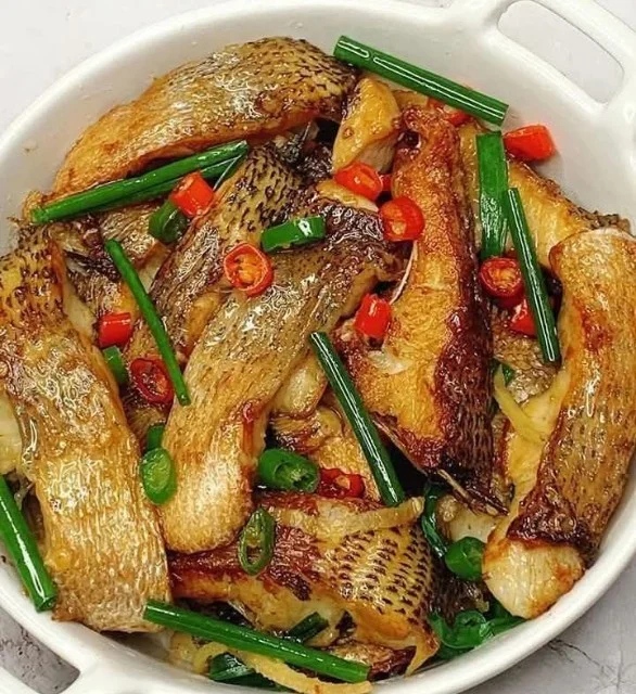 Pan-fried fish garnished with ginger and scallions on a white plate.