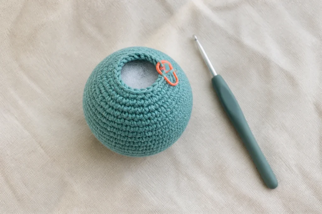 Unfinished teal amigurumi piece with stuffing and stitch marker